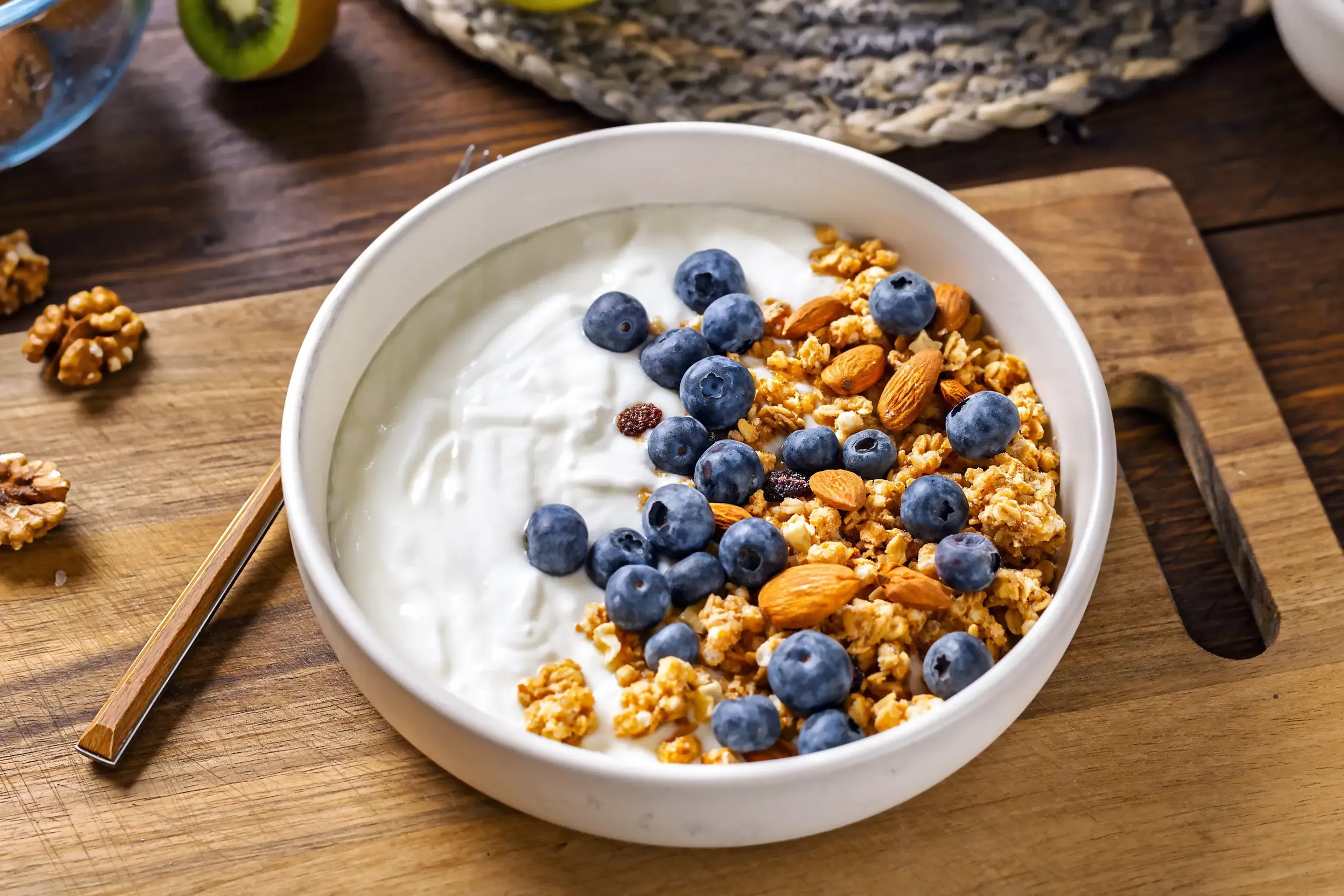 Bowl with greek yogurt, granola, almonds, walnuts and blueberries on wooden table.